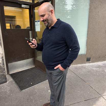 Man outside an office building in the dark blue Bleamme Long Sleeve Knit Polo with grey trousers