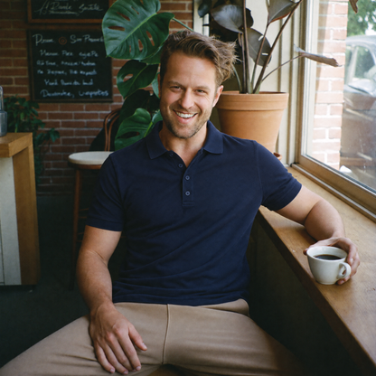 Man relaxing at a café window with a coffee in the navy Bleamme Short Sleeve Polo