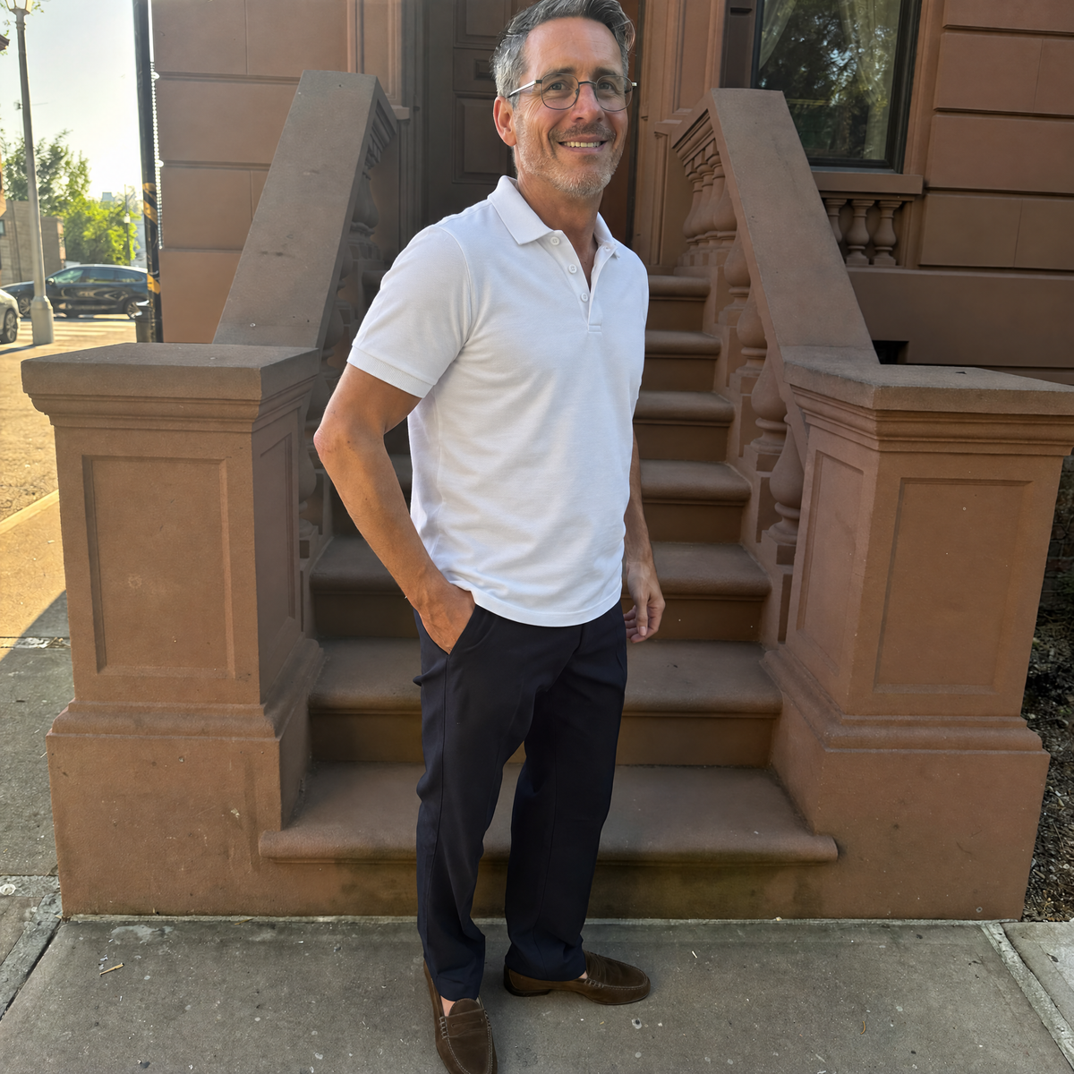 Man on brownstone steps in the white Bleamme Short Sleeve Polo with navy chinos and loafers